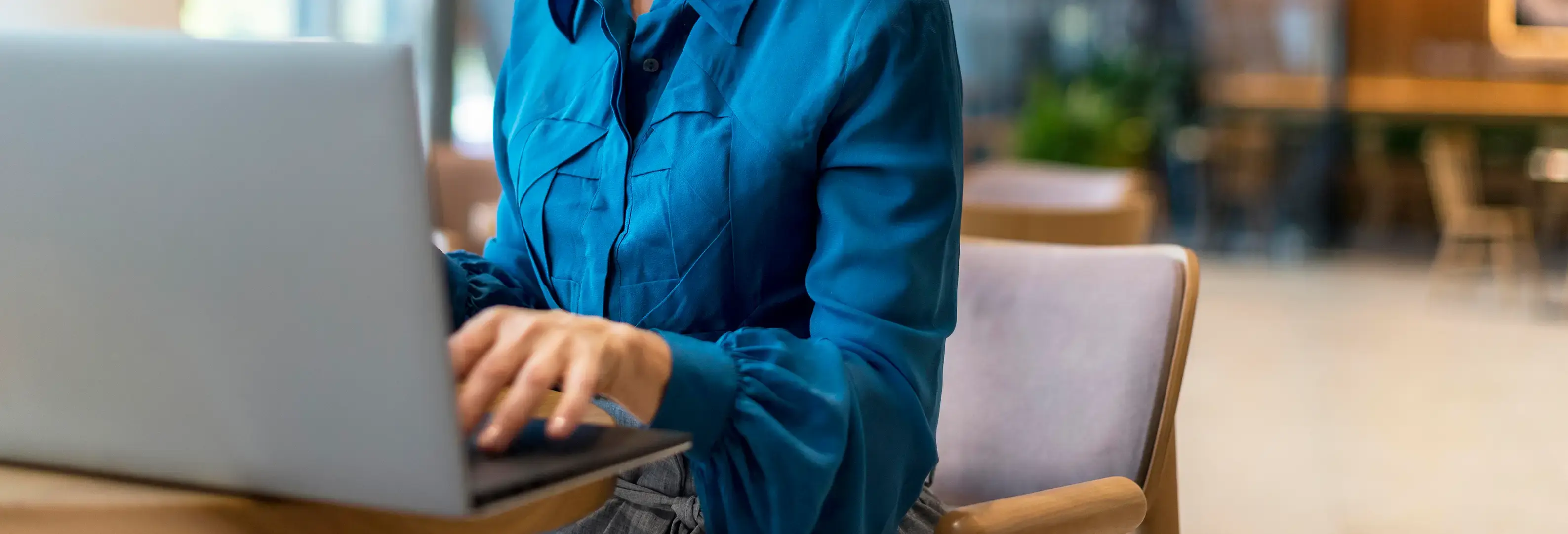 Γυναίκα κάθεται σε καρέκλα και χρησιμοποιεί φορητό υπολογιστή.