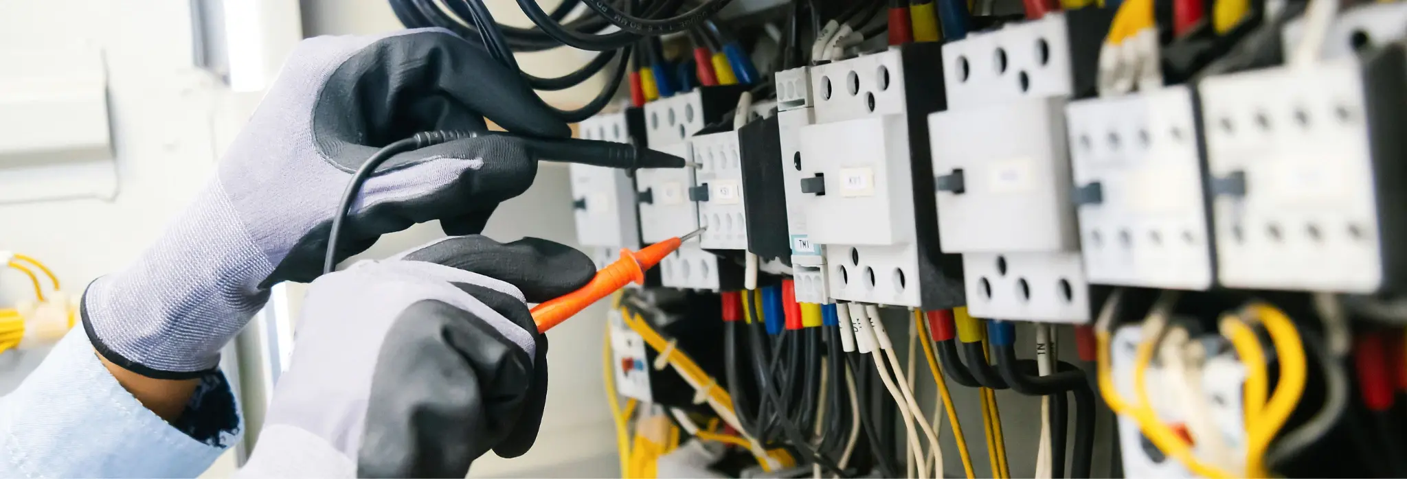 Ηλεκτρολόγος με γάντια ασφαλείας χρησιμοποιεί πολύμετρο για να ελέγξει ηλεκτρικό πίνακα.