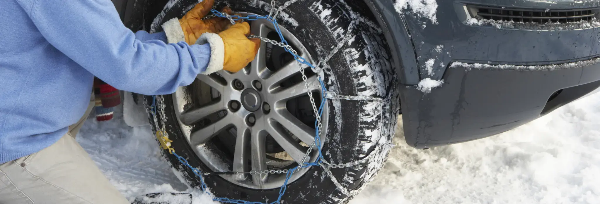 Άνθρωπος με γάντια τοποθετεί αλυσίδες χιονιου στο λάστιχο αυτοκινήτου.