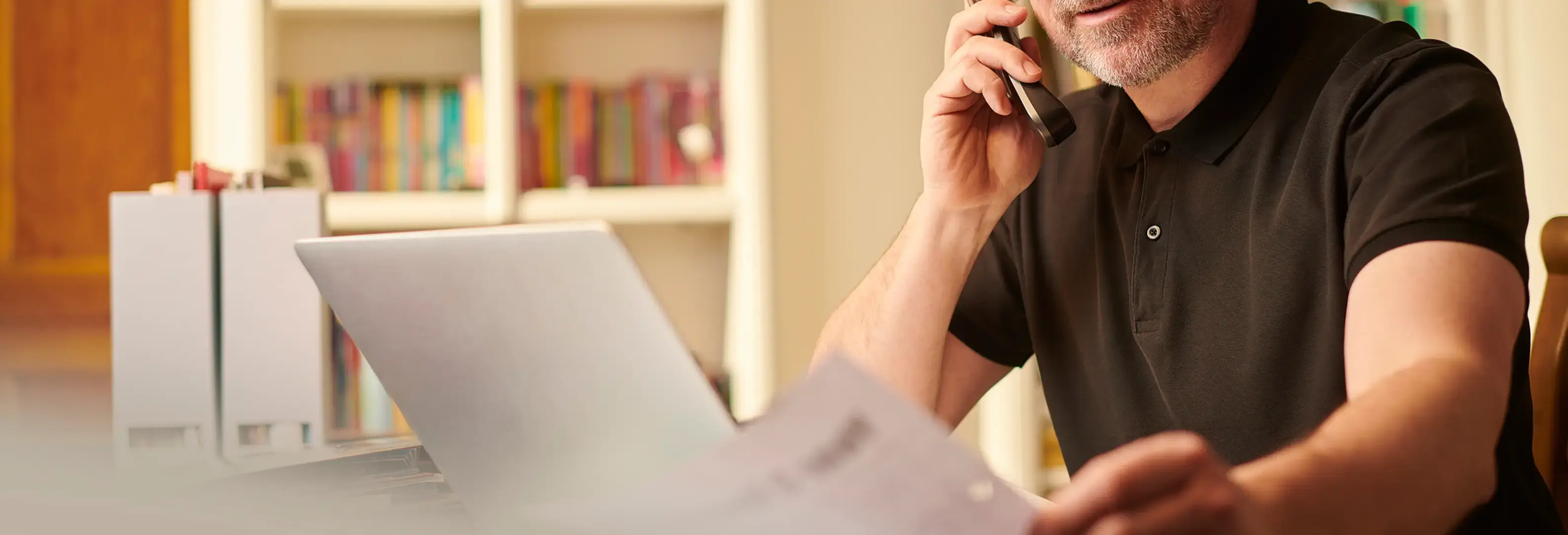 Άντρας μιλάει στο τηλέφωνο μπροστά από laptop και κρατάει λογαριασμό.