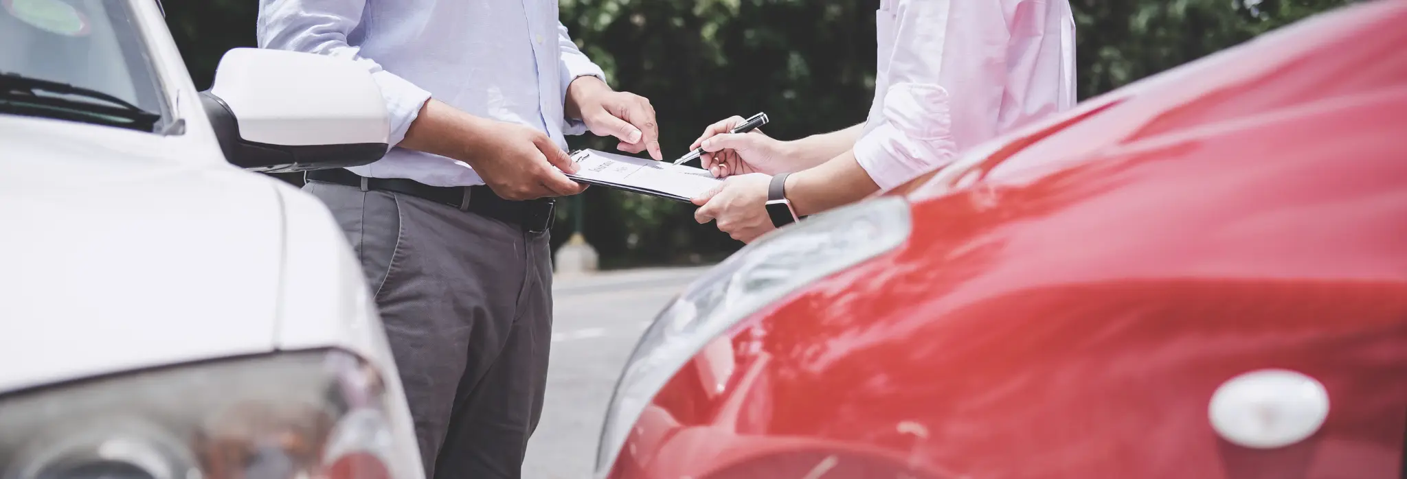 Δύο οδηγοί ανάμεσα σε λευκό και κόκκινο αυτοκίνητο κάνουν δήλωση τροχαίου για ασφαλιστική κάλυψη μετά από μικρή σύγκρουση.