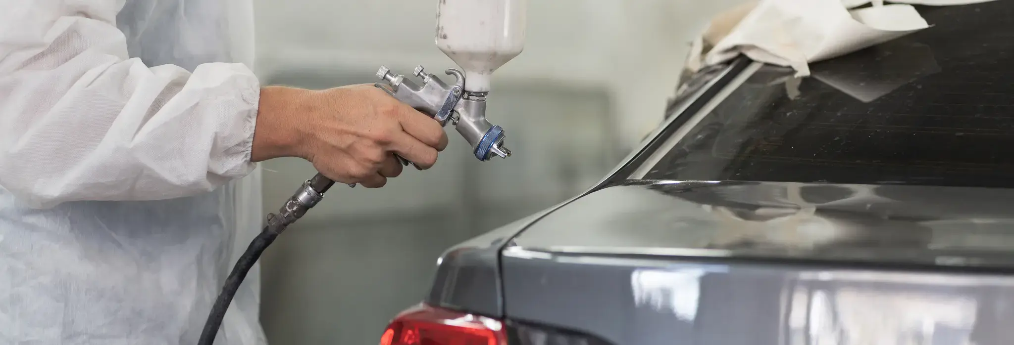 Χέρι κρατάει σπρει βαψίματος και βάφει ένα αυτοκίνητο.