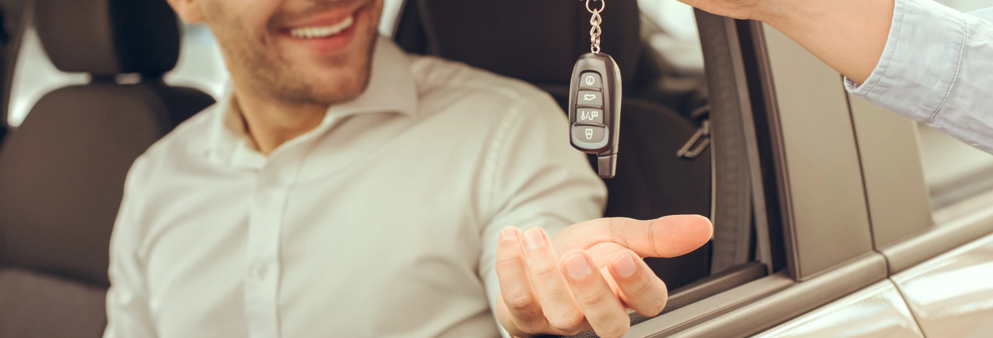 Ένα χέρι παραδίδει κλειδί αυτοκινήτου σε χαμογελαστό άντρα που κάθεται στη θέση του οδηγού.