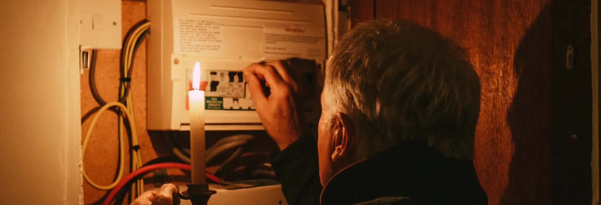 Άντρας με κερί ανεβάζει πεσμένη ασφάλεια από διακοπή ρεύματος.