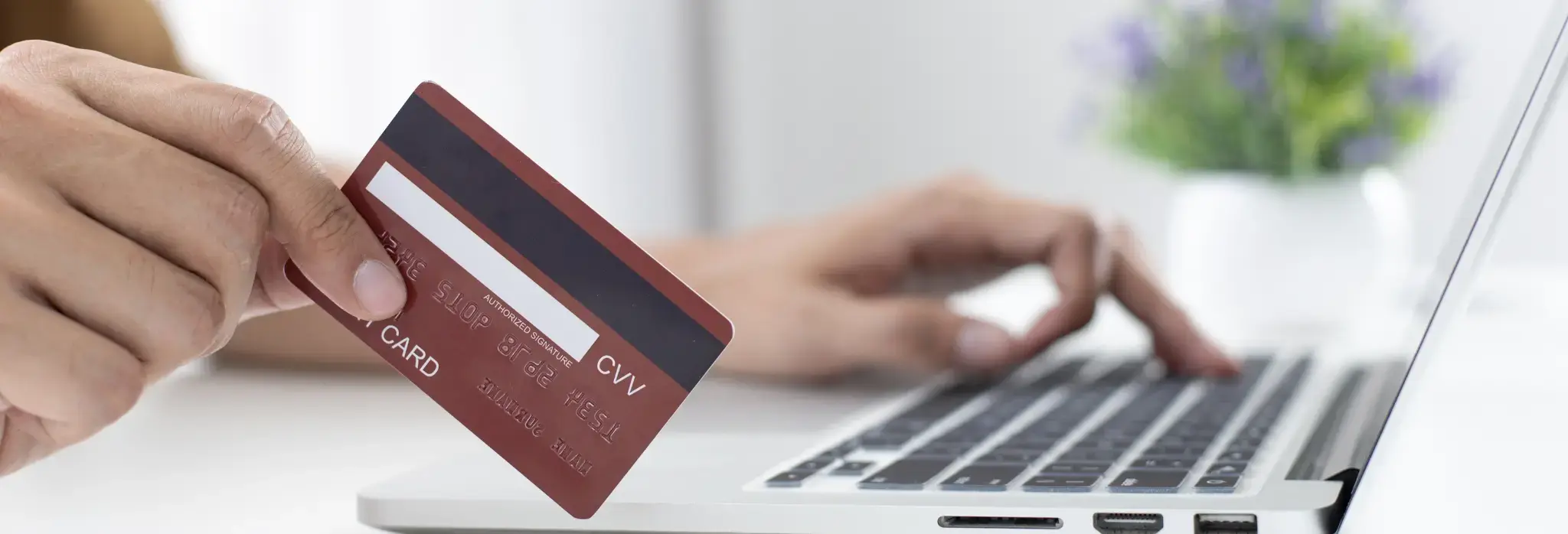 Χέρι που κρατά πιστωτική κάρτα ενώ πληκτρολογεί σε φορητό υπολογιστή για ηλεκτρονική πληρωμή.