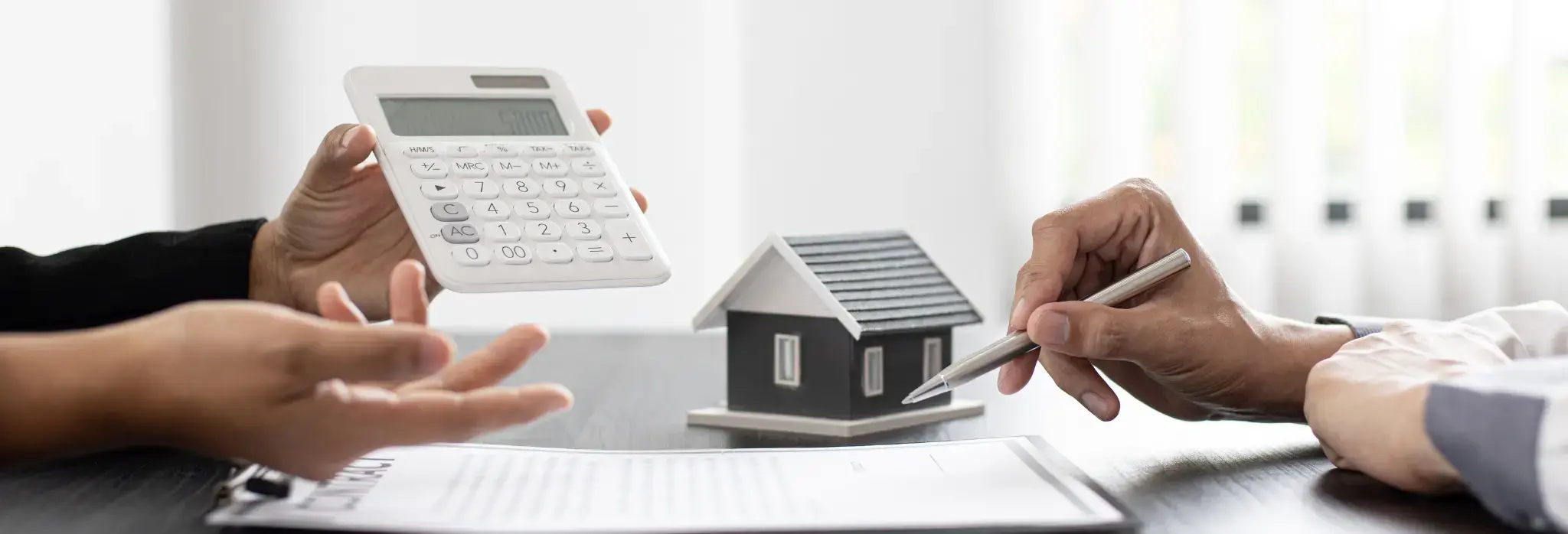 Δύο άνθρωποι σε τραπέζι με κομπιουτεράκι, χαρτιά και ένα μικρό σπιτάκι.