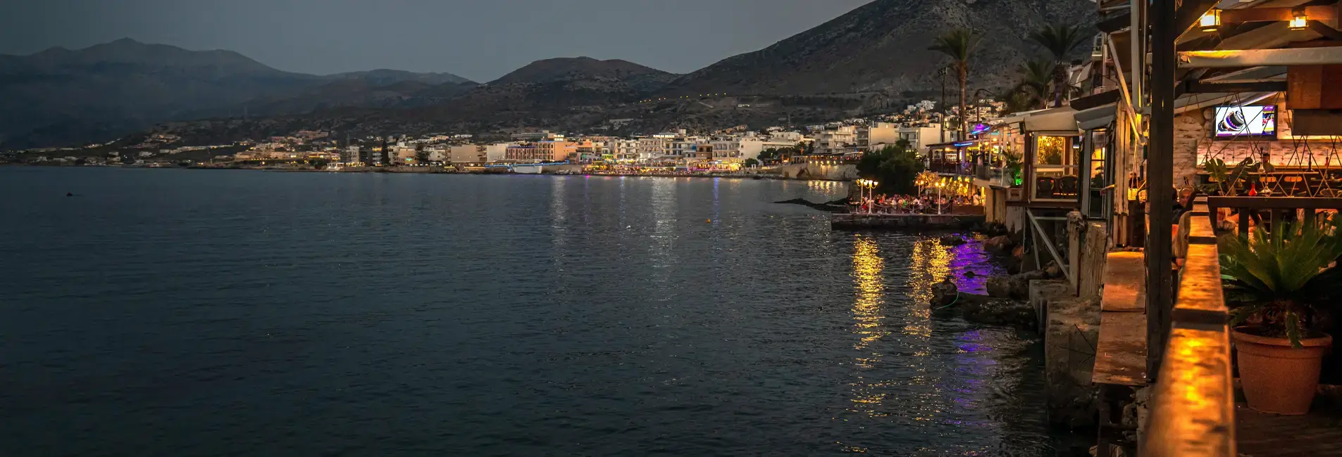 Παραθαλάσσια περιοχή, με εστιατόρια και μπαρ κατά μήκος της ακτής και φώτα να καθρεφτίζονται στη θάλασσα.