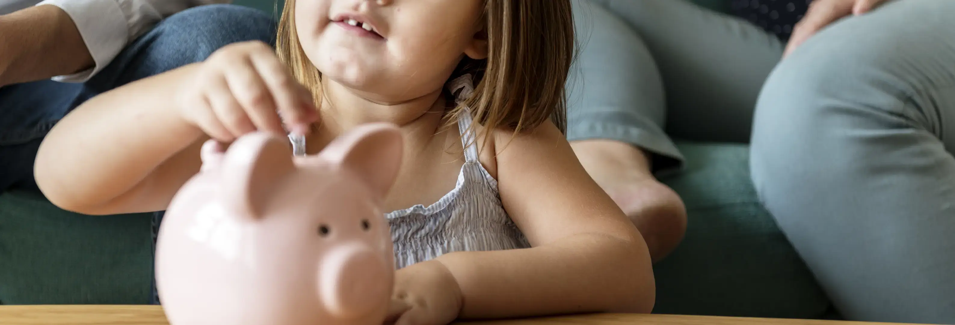 Μικρό κοριτσάκι βάζει κέρμα σε κουμπαρά σε σχήμα γουρουνάκι.