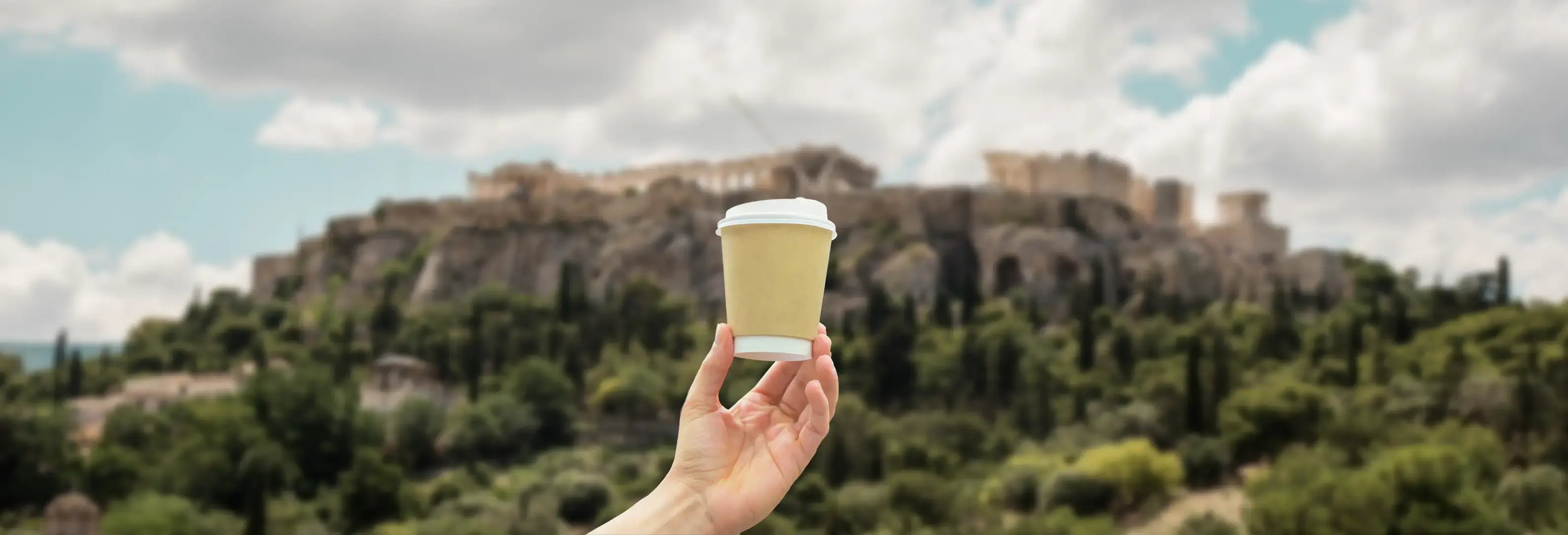 Χέρι κρατάει καφέ με θέα την Ακρόπολη στην Αθήνα.