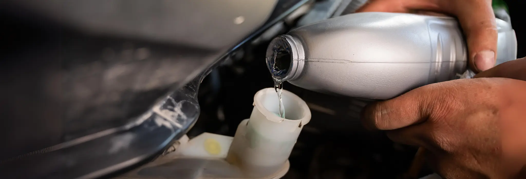 Χέρια που κρατάνε μπουκάλι με υγρό φρένων και το τοποθετούν στην αντλία.