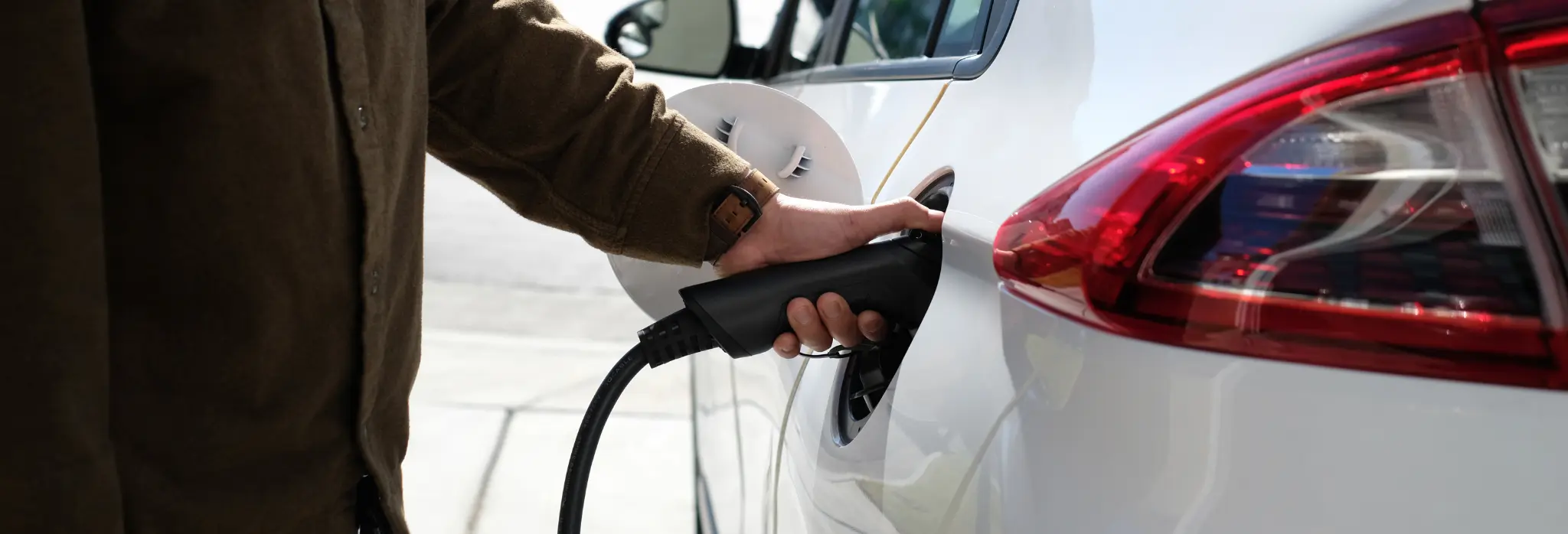 Άντρας τοποθετεί φορτιστή σε ηλεκτρικό αυτοκίνητο.