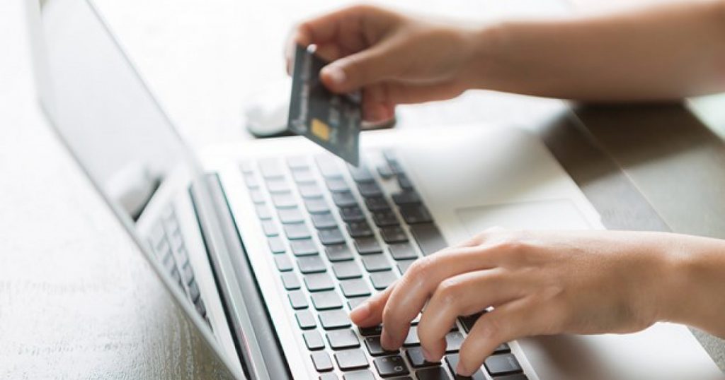 Χέρια σε φορητό υπολογιστή πραγματοποιούν ηλεκτρονική πληρωμή με κάρτα.