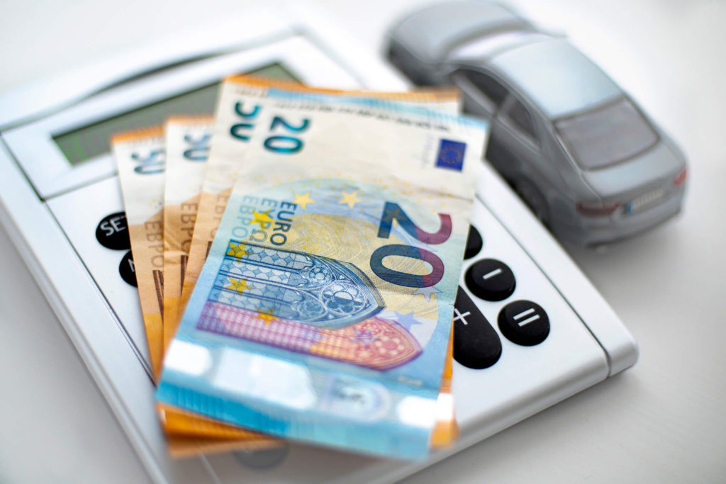 Χαρτονομίσματα των 50€ και των 20€ πάνω σε κομπιουτεράκι δίπλα από μινιατούρα αυτοκίνητο.